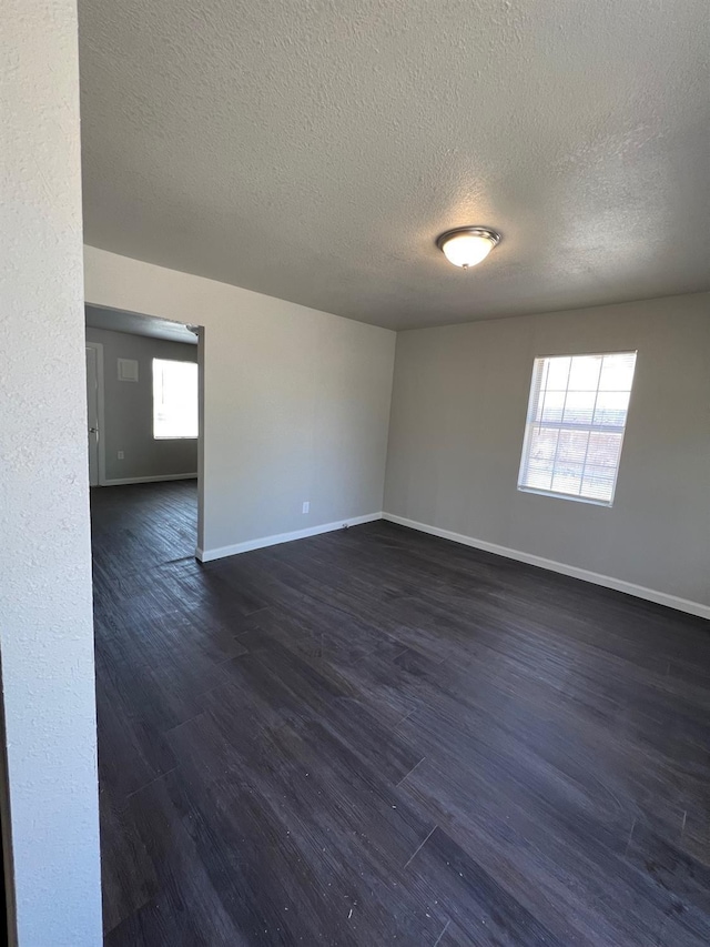 spare room featuring a healthy amount of sunlight, dark hardwood / wood-style flooring, and a textured ceiling