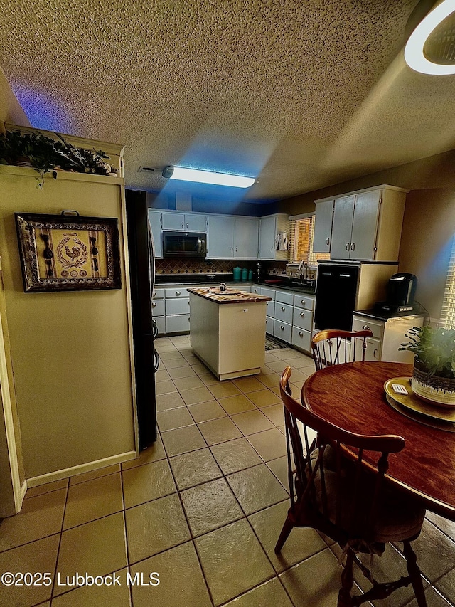 5226 92nd St, Lubbock, TX 79424 - kitchen with dark countertops, light tile patterned floors, freestanding refrigerator, a textured ceiling, and tasteful backsplash