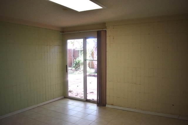 spare room featuring light tile patterned flooring, a skylight, and tile walls