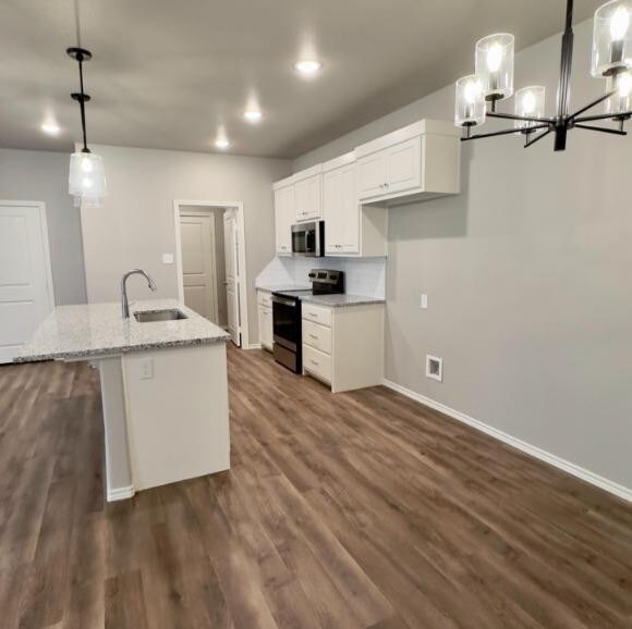 kitchen featuring light stone counters, sink, an island with sink, pendant lighting, and appliances with stainless steel finishes