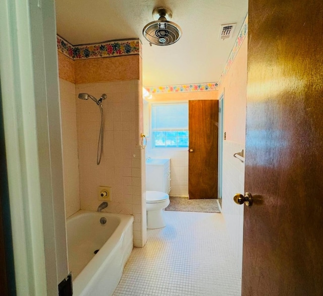 bathroom with tile patterned floors, toilet, tiled shower / bath combo, and tile walls