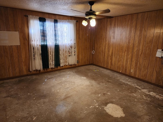 empty room with ceiling fan, a textured ceiling, and wood walls