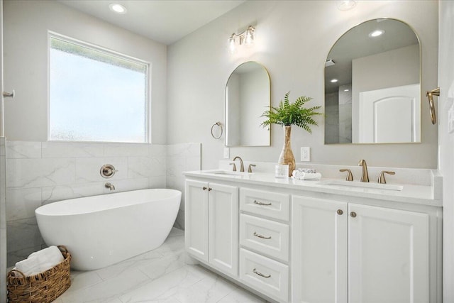 1403 Durham Ave, Wolfforth, TX 79382 - bathroom featuring marble look tile flooring, double vanity, a freestanding tub, tile walls, and a wainscoted wall