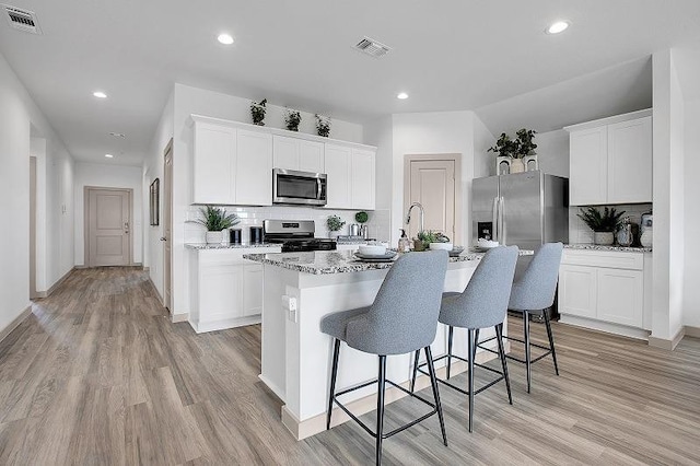 kitchen featuring decorative backsplash, stainless steel appliances, white cabinets, and a center island with sink