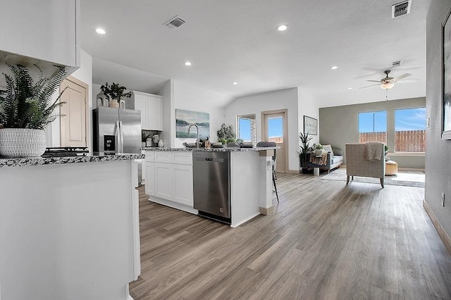 kitchen with light hardwood / wood-style flooring, a breakfast bar, stainless steel appliances, light stone counters, and white cabinets