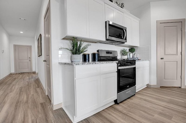 kitchen with stainless steel appliances, white cabinets, backsplash, and light hardwood / wood-style floors