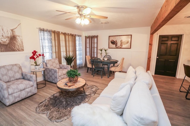 living room with wood-type flooring, ornamental molding, and ceiling fan