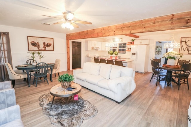 living room featuring beamed ceiling, ceiling fan, ornamental molding, and light wood-type flooring