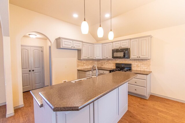 kitchen featuring tasteful backsplash, light hardwood / wood-style flooring, black appliances, and a center island with sink