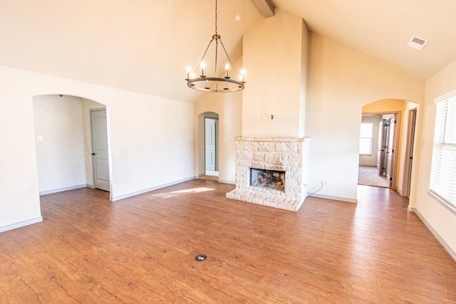 unfurnished living room with a stone fireplace, hardwood / wood-style floors, high vaulted ceiling, a notable chandelier, and beam ceiling