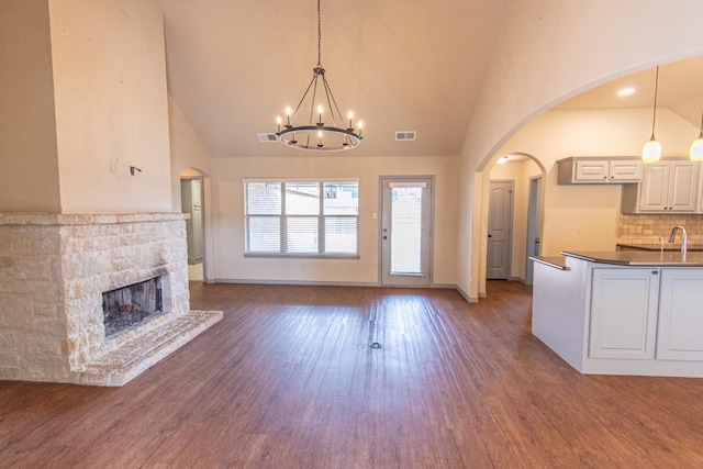 unfurnished living room featuring a stone fireplace, sink, a notable chandelier, and dark hardwood / wood-style floors