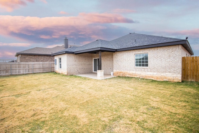 back house at dusk featuring a patio and a lawn