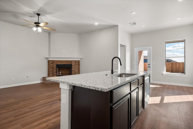 kitchen featuring a fireplace, dishwasher, sink, dark wood-type flooring, and a center island with sink