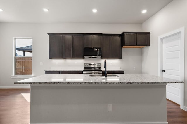 kitchen with light stone counters, sink, stainless steel appliances, and a center island with sink