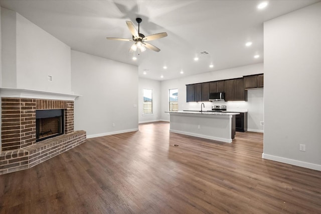 unfurnished living room featuring a brick fireplace, dark hardwood / wood-style floors, and ceiling fan