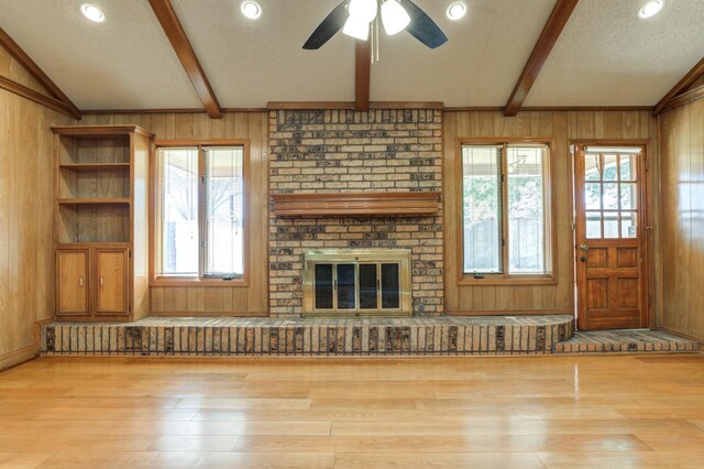 unfurnished living room featuring a brick fireplace, wooden walls, and a healthy amount of sunlight