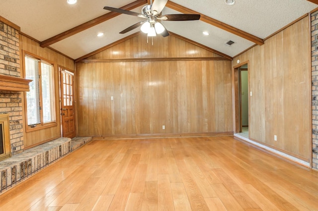 unfurnished living room featuring light hardwood / wood-style floors, vaulted ceiling with beams, wooden walls, and a fireplace