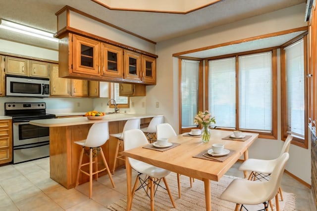 kitchen with appliances with stainless steel finishes, light tile patterned floors, sink, a kitchen bar, and kitchen peninsula