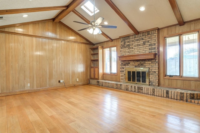 unfurnished living room featuring a fireplace, light wood-type flooring, vaulted ceiling with skylight, and wood walls