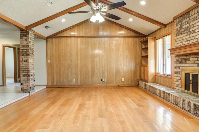 unfurnished living room featuring light wood-type flooring, wood walls, lofted ceiling with beams, decorative columns, and a brick fireplace