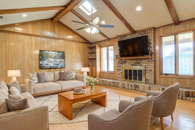 living room with light hardwood / wood-style floors, lofted ceiling with skylight, a brick fireplace, and wooden walls