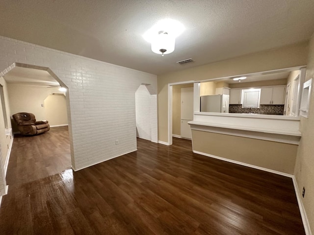 unfurnished living room featuring brick wall, dark hardwood / wood-style floors, and a textured ceiling