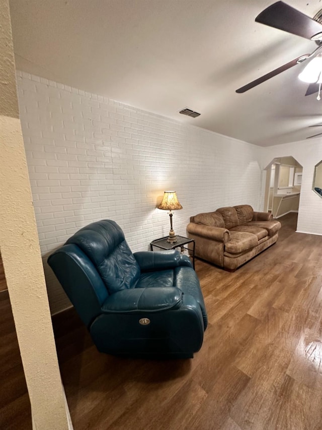 living room featuring hardwood / wood-style flooring, ceiling fan, and brick wall