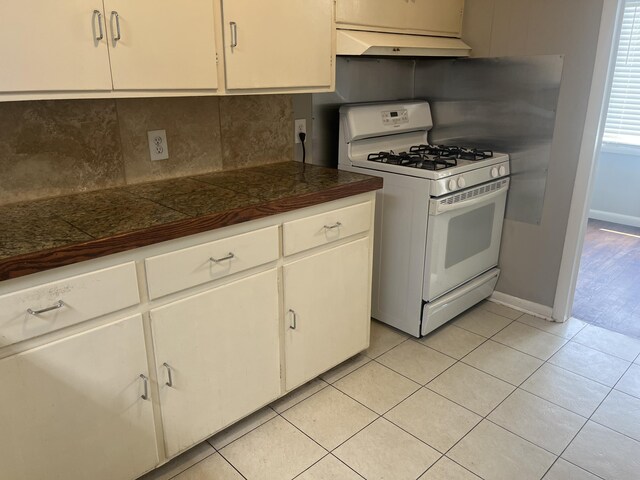 2602 45th St, Lubbock, TX 79413 - kitchen with gas range gas stove, custom exhaust hood, tasteful backsplash, light tile patterned floors, and tile countertops