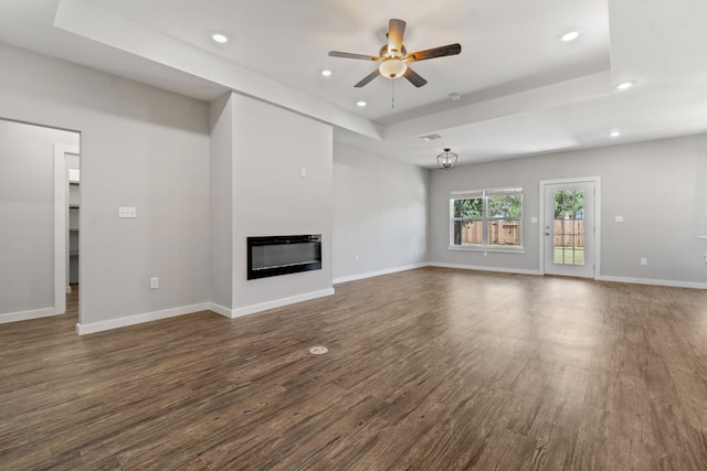 unfurnished living room with dark hardwood / wood-style floors, ceiling fan, and a tray ceiling