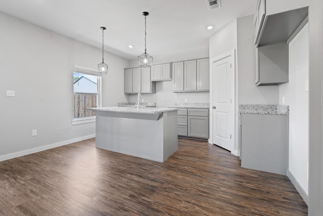 kitchen featuring pendant lighting, an island with sink, gray cabinetry, light stone countertops, and dark wood-type flooring