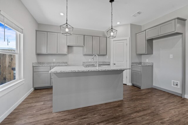 kitchen with light stone counters, a kitchen island with sink, sink, and gray cabinetry