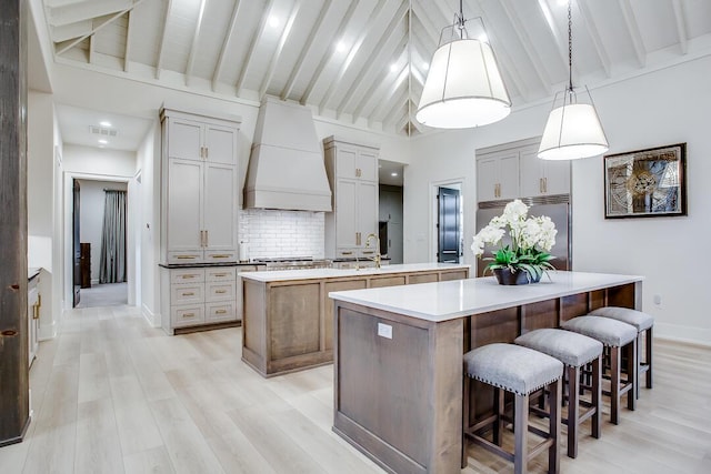 4821 119th Pl, Lubbock, TX 79424 - kitchen featuring an island with sink, custom exhaust hood, appliances with stainless steel finishes, tasteful backsplash, and light wood-style flooring