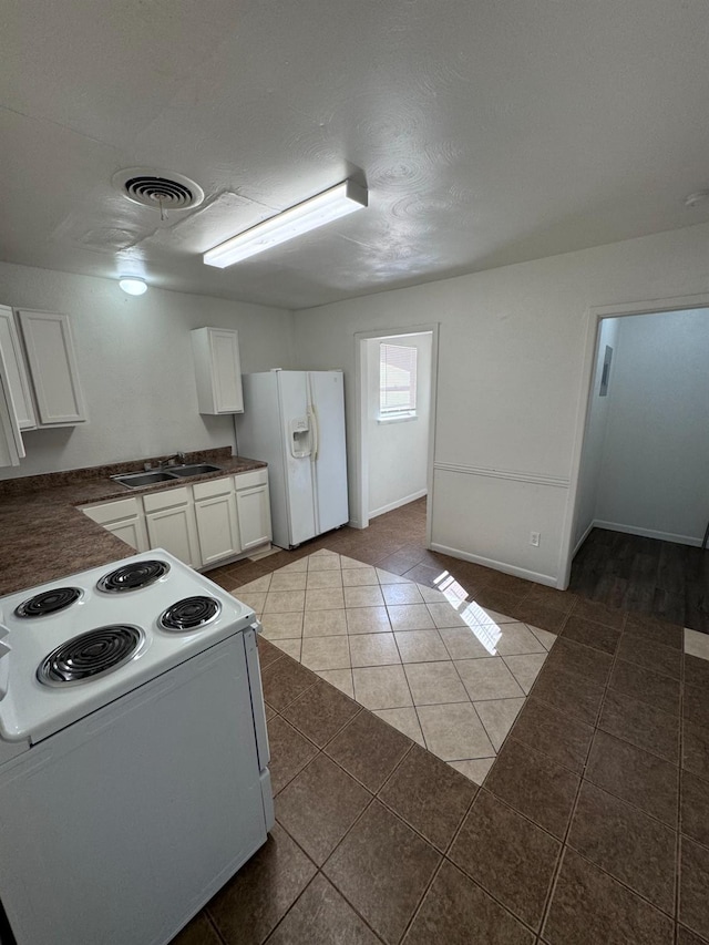 kitchen with sink, a textured ceiling, dark tile patterned flooring, white appliances, and white cabinets