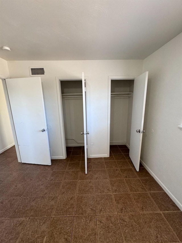 unfurnished bedroom featuring two closets and dark tile patterned floors