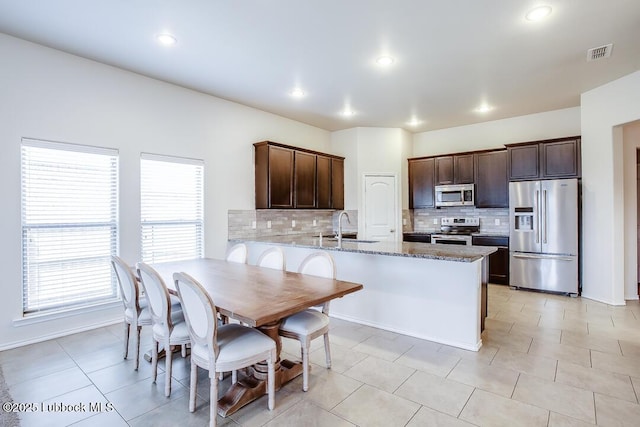 3404 Saratoga Ave, Lubbock, TX 79407 - kitchen featuring appliances with stainless steel finishes, backsplash, dark brown cabinetry, a peninsula, and light stone counters