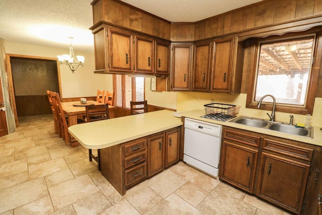 kitchen featuring a wealth of natural light, decorative light fixtures, sink, white dishwasher, and kitchen peninsula