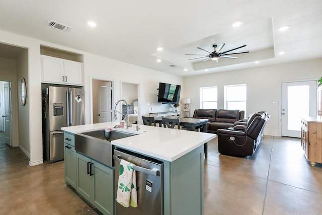 kitchen with sink, concrete flooring, stainless steel appliances, a tray ceiling, and an island with sink