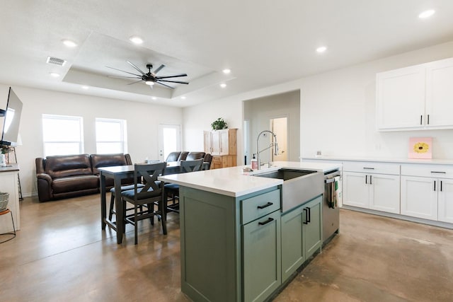 kitchen featuring a kitchen island with sink, sink, white cabinetry, and a tray ceiling