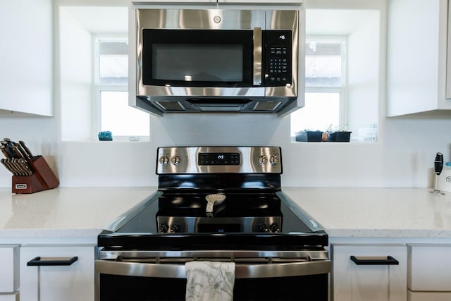 kitchen with white cabinetry, light stone counters, stainless steel appliances, and a healthy amount of sunlight