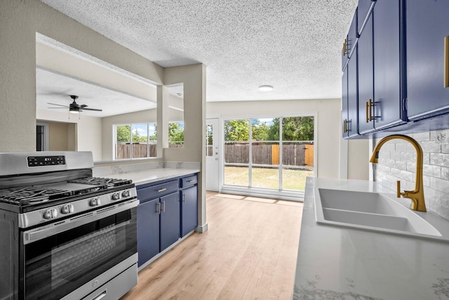 kitchen with blue cabinetry, sink, stainless steel gas range oven, a textured ceiling, and light hardwood / wood-style floors