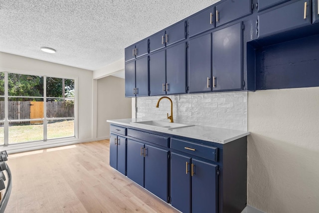 kitchen with sink, light hardwood / wood-style flooring, backsplash, a textured ceiling, and blue cabinets