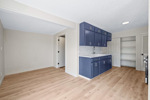 kitchen featuring sink, a textured ceiling, blue cabinetry, and light wood-type flooring