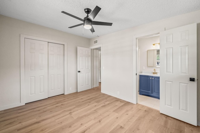 unfurnished bedroom with connected bathroom, sink, a textured ceiling, light wood-type flooring, and a closet