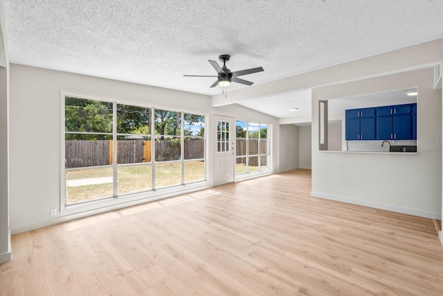 unfurnished living room with lofted ceiling, sink, ceiling fan, a textured ceiling, and light hardwood / wood-style flooring