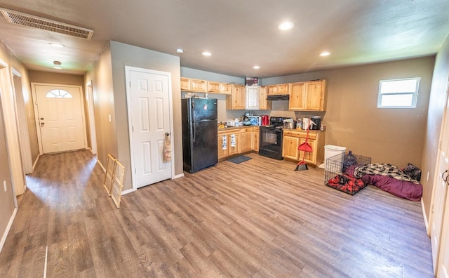 kitchen featuring light brown cabinetry, light hardwood / wood-style floors, and black appliances