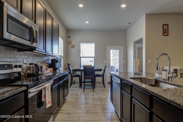 10423 Winfield Ave, Lubbock, TX 79424 - kitchen featuring appliances with stainless steel finishes, a sink, dark stone countertops, recessed lighting, and light wood-style floors
