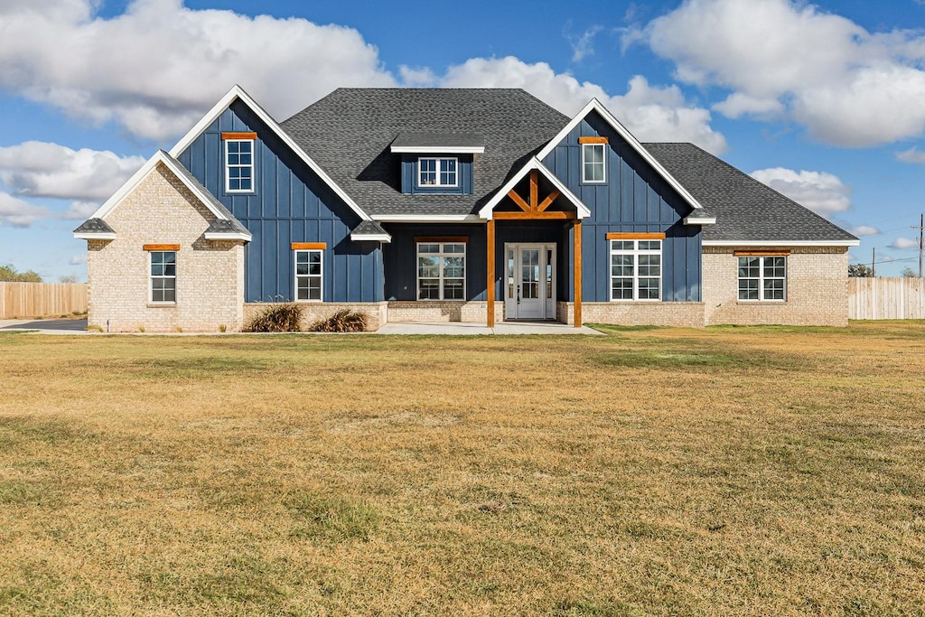 view of front facade with board and batten siding, roof with shingles, a front lawn, and fence