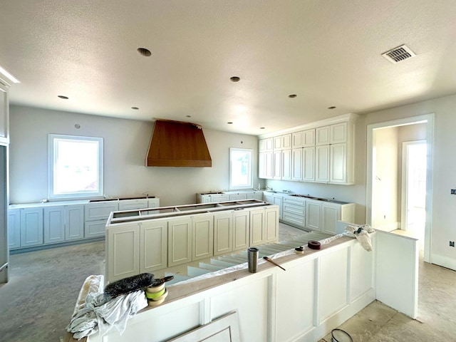 kitchen with white cabinetry, a textured ceiling, and wall chimney exhaust hood