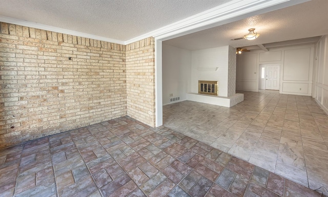 empty room with brick wall, a fireplace, and a textured ceiling