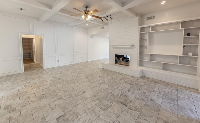 unfurnished living room featuring built in features, beamed ceiling, coffered ceiling, ceiling fan, and a brick fireplace